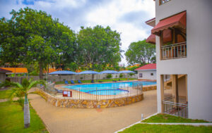 The best gated communities in Ghana - This image shows a section of the Regimanuel Clubhouse swimming pool with trees dotted around it to provide shade and beautiful lawns around the pool area.