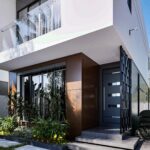 A house for sale on off-plan installment - This is a white 2 bedroom semi-detached house at Regimanuel Satellite City at East Legon Hills showing the frontage with a wooden facade and parking space.